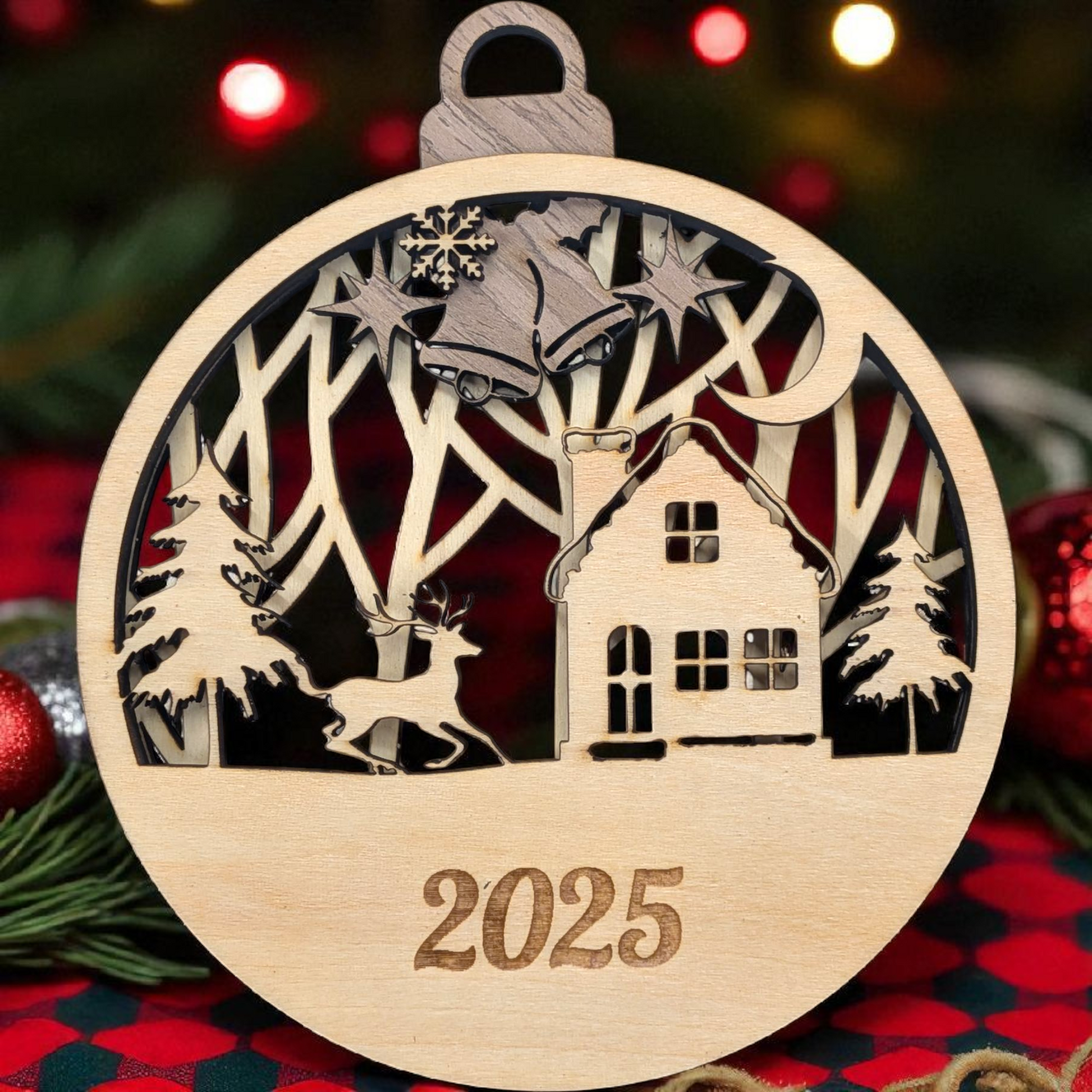 Wooden Christmas ornament with cut-out design of a house, trees, and deer, with '2025' engraved, on a festive background.