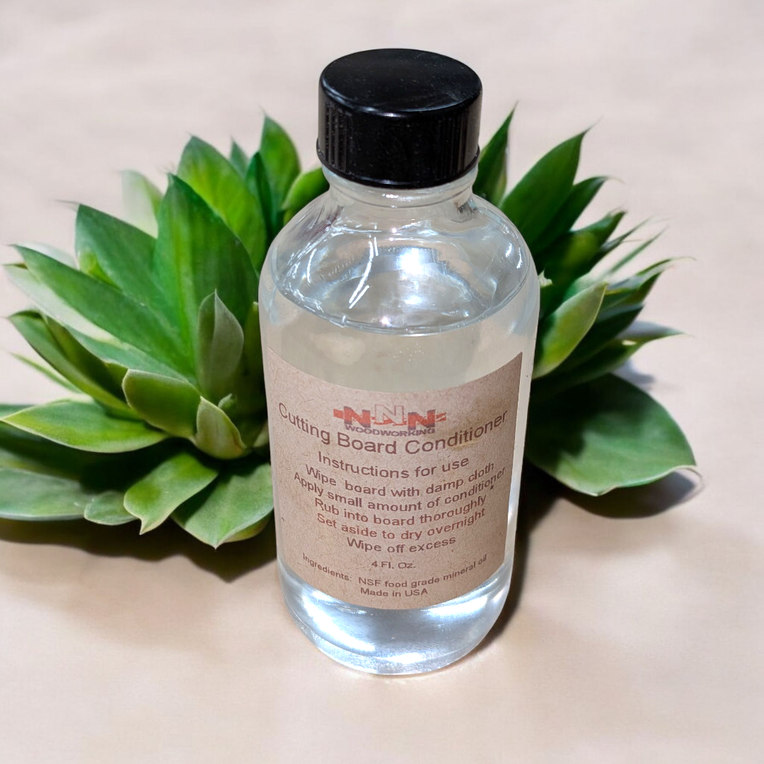 Bottle of cutting board conditioner with a black cap on a beige background with green leaves.