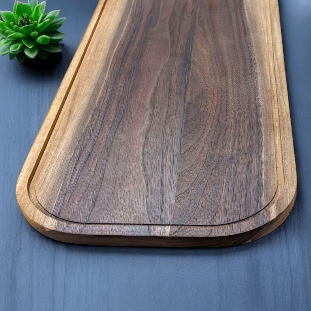 Wooden walnut cutting board on a blue surface with a small green plant.