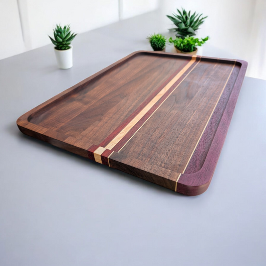 Wooden walnut cutting board with a striped design on a light gray surface with small potted plants in the background.
